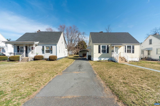 bungalow featuring a shingled roof, a front lawn, aphalt driveway, covered porch, and a chimney