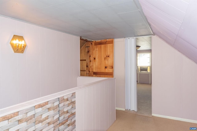 hall featuring lofted ceiling, wood walls, and light carpet