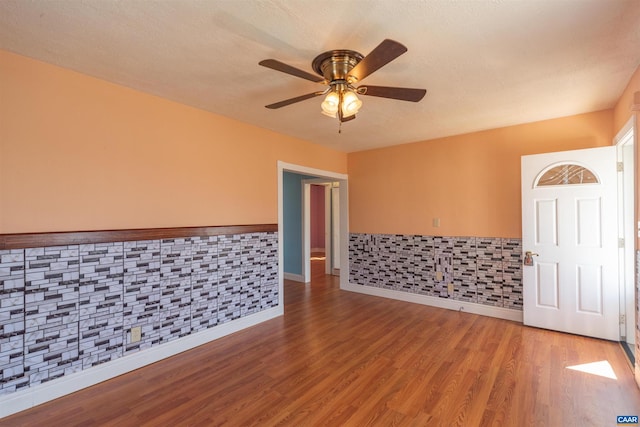 spare room with light wood finished floors, a wainscoted wall, a textured ceiling, and a ceiling fan