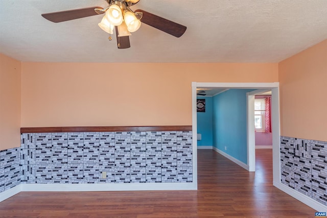 empty room featuring ceiling fan, wood finished floors, a wainscoted wall, and a textured ceiling