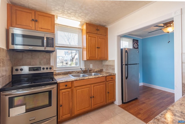 kitchen featuring a sink, decorative backsplash, stainless steel appliances, crown molding, and brown cabinets