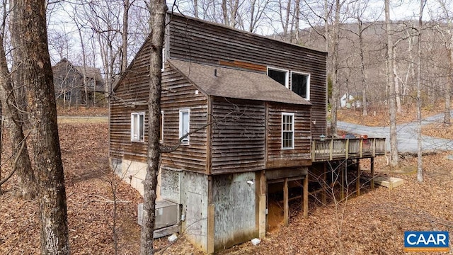 view of side of property with a deck, central AC unit, and a shingled roof