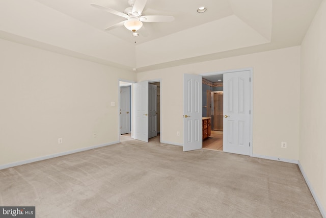 unfurnished bedroom featuring baseboards, ensuite bath, recessed lighting, a raised ceiling, and light colored carpet