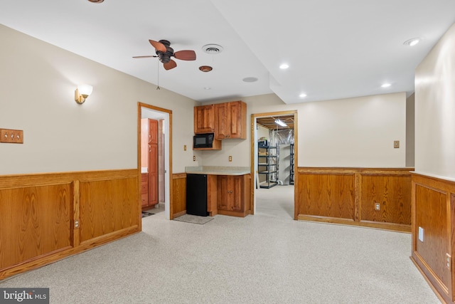 kitchen featuring brown cabinetry, a wainscoted wall, black microwave, and ceiling fan