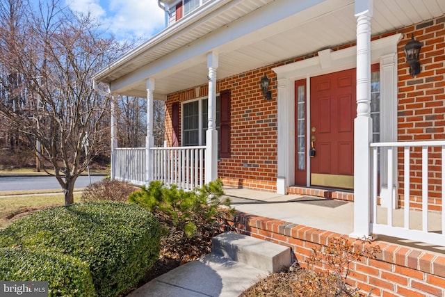 view of exterior entry with brick siding and covered porch