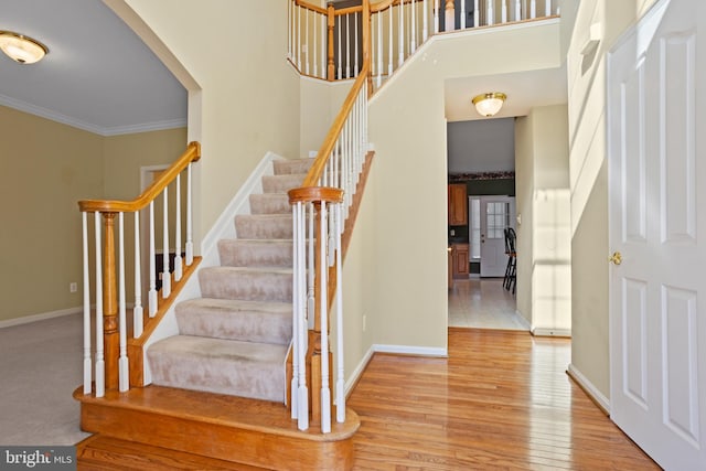 stairs with a high ceiling, wood finished floors, baseboards, and ornamental molding