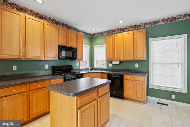 kitchen featuring dark countertops, a kitchen island, baseboards, black appliances, and a sink