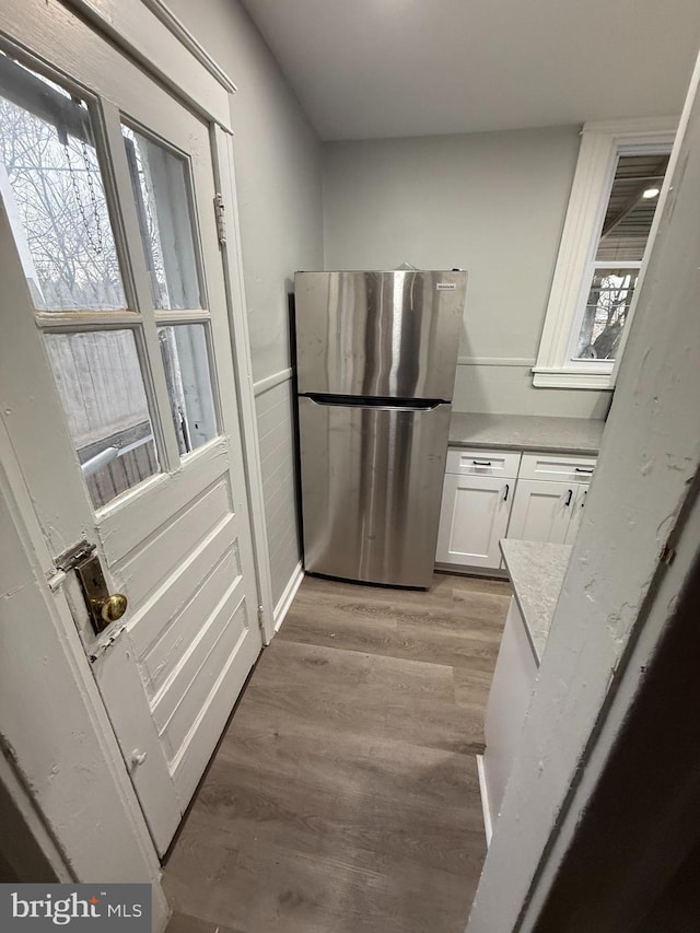 kitchen featuring white cabinets, light wood-type flooring, freestanding refrigerator, and light countertops