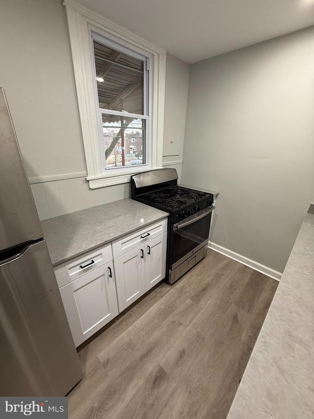 kitchen with tasteful backsplash, white cabinetry, stainless steel appliances, light wood-style floors, and light countertops