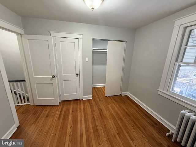 unfurnished bedroom with a closet, radiator heating unit, baseboards, and wood finished floors