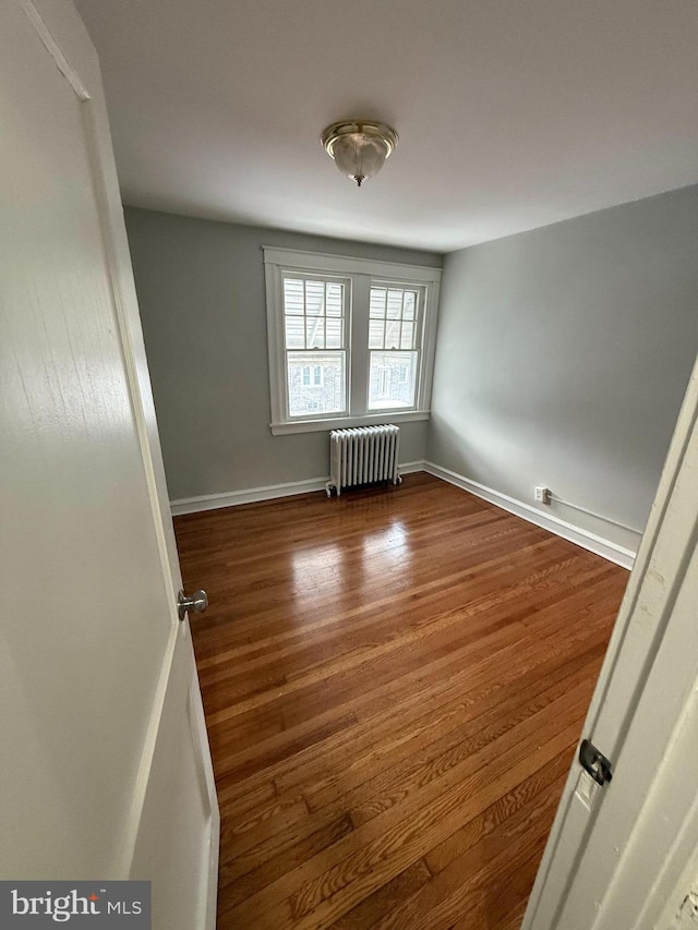 spare room featuring baseboards, wood finished floors, and radiator heating unit