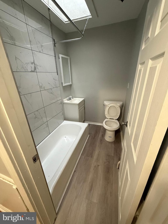 full bathroom with wood finished floors, baseboards, a skylight, shower / bathing tub combination, and toilet