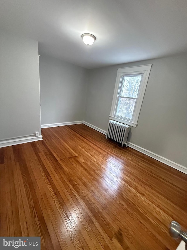 spare room featuring hardwood / wood-style floors, radiator, and baseboards