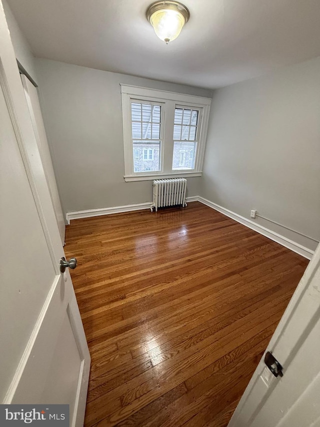 spare room featuring radiator heating unit, wood finished floors, and baseboards