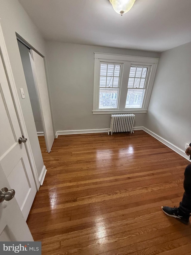 unfurnished bedroom featuring a closet, radiator heating unit, baseboards, and wood finished floors