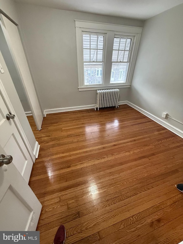 unfurnished room featuring baseboards, wood finished floors, and radiator heating unit