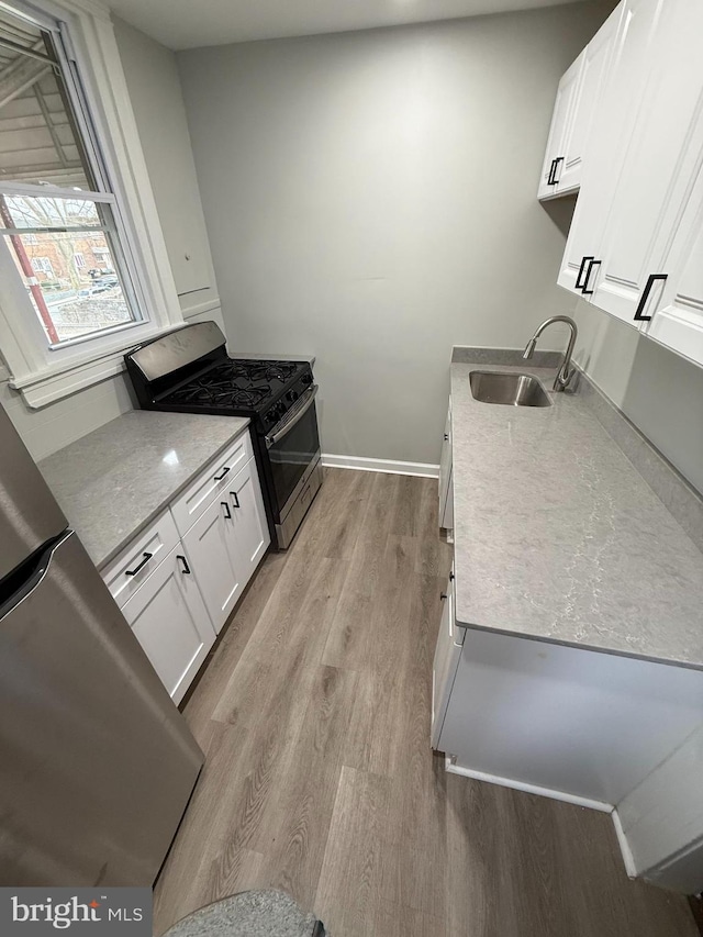 kitchen with baseboards, a sink, white cabinets, light wood-style floors, and appliances with stainless steel finishes