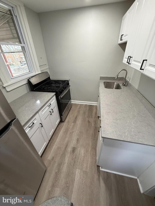 kitchen with light wood finished floors, baseboards, stainless steel gas stove, white cabinetry, and a sink