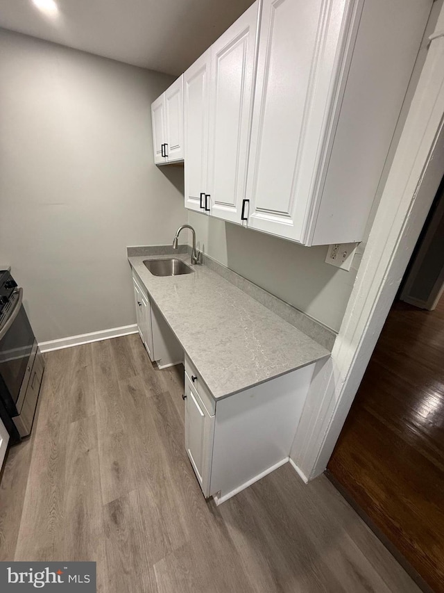 interior space with wood finished floors, a sink, light countertops, white cabinetry, and range