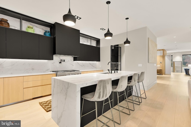 kitchen with wall chimney range hood, light brown cabinetry, dark cabinetry, modern cabinets, and a sink