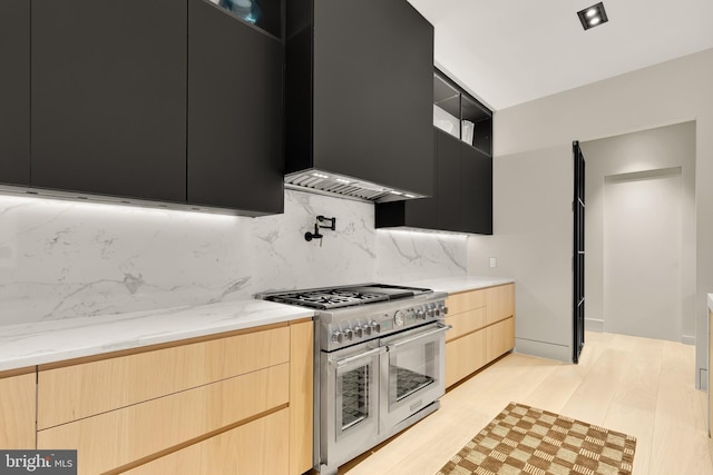 kitchen with light wood-style flooring, light brown cabinets, double oven range, wall chimney exhaust hood, and dark cabinets