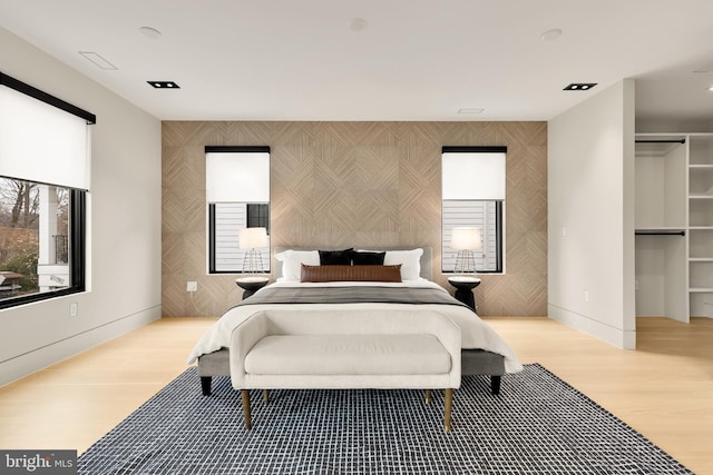 bedroom with light wood finished floors, wallpapered walls, an accent wall, and baseboards