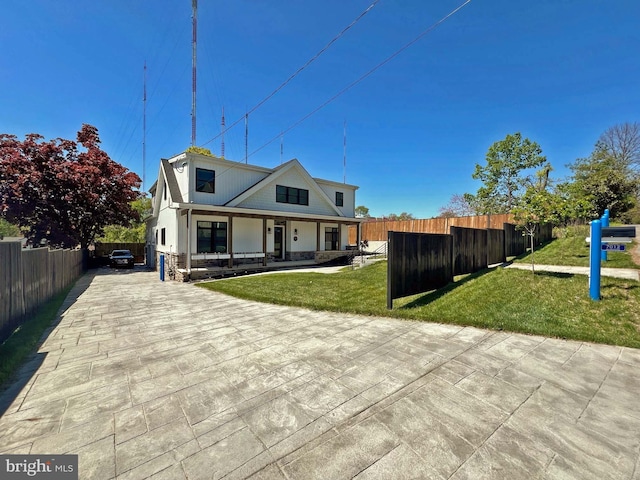 back of property with a yard, stone siding, covered porch, and fence