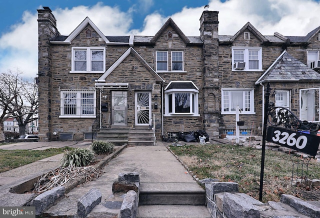 view of front facade featuring stone siding, cooling unit, and a chimney