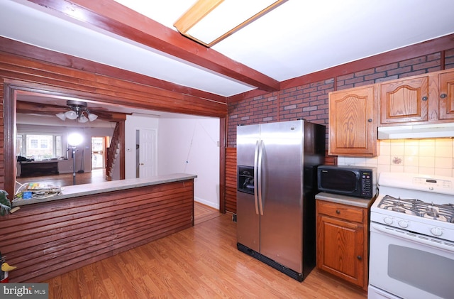 kitchen with beam ceiling, stainless steel refrigerator with ice dispenser, under cabinet range hood, white gas range oven, and black microwave