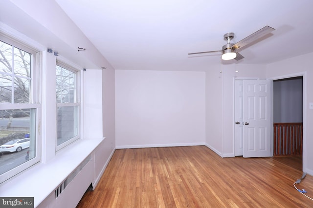 unfurnished room featuring a ceiling fan, radiator, light wood-style floors, and baseboards