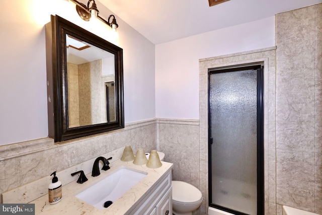 full bath featuring toilet, vanity, wainscoting, a stall shower, and tile walls