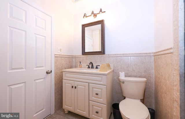 bathroom with a wainscoted wall, toilet, vanity, and tile walls