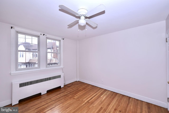 empty room featuring baseboards, light wood-style floors, ceiling fan, and radiator heating unit