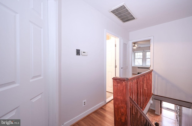 hall featuring visible vents, baseboards, an upstairs landing, and light wood finished floors