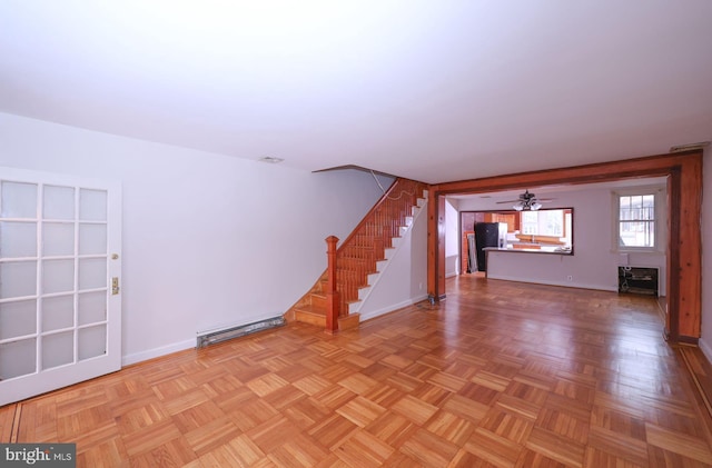 unfurnished living room featuring stairs, a ceiling fan, baseboards, and a baseboard radiator