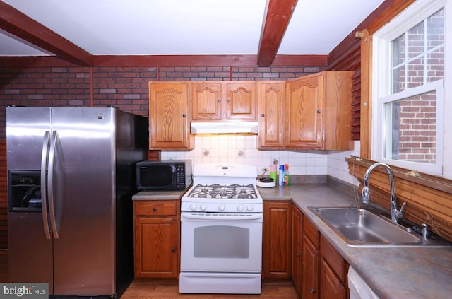 kitchen with tasteful backsplash, under cabinet range hood, beam ceiling, white appliances, and a sink