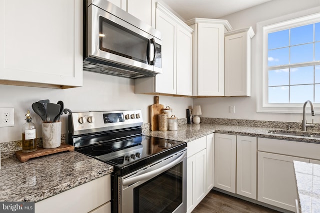 kitchen with a sink, light stone countertops, appliances with stainless steel finishes, white cabinetry, and dark wood-style flooring