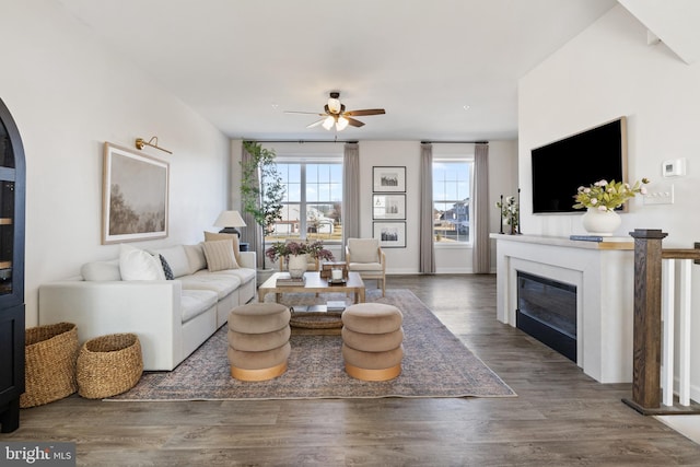 living room featuring a glass covered fireplace, wood finished floors, and a ceiling fan