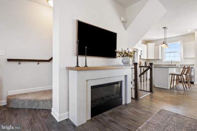 living area featuring a glass covered fireplace, baseboards, dark wood-style floors, and recessed lighting