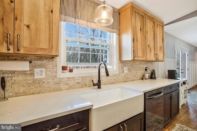 kitchen featuring a sink, wood finished floors, light countertops, decorative backsplash, and dishwasher