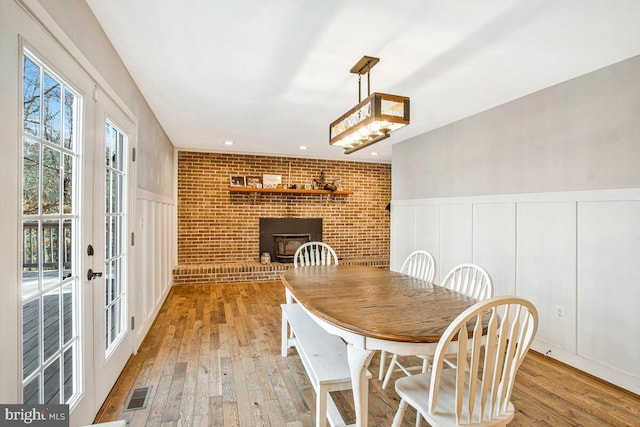 dining room featuring light wood finished floors, visible vents, brick wall, wainscoting, and a decorative wall