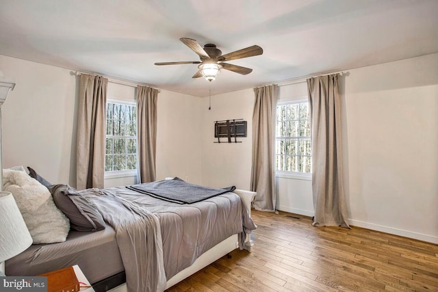 bedroom with multiple windows, wood-type flooring, baseboards, and a ceiling fan