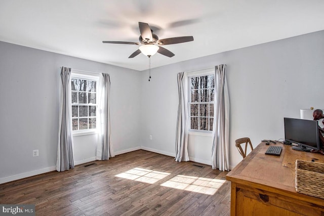 unfurnished office featuring a ceiling fan, visible vents, wood finished floors, and baseboards