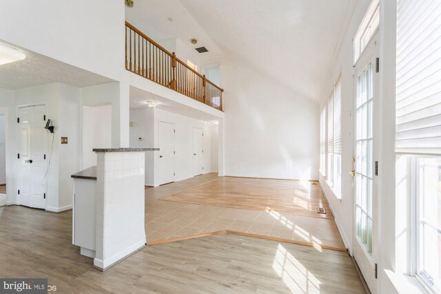unfurnished living room featuring light wood finished floors, high vaulted ceiling, a ceiling fan, baseboards, and visible vents