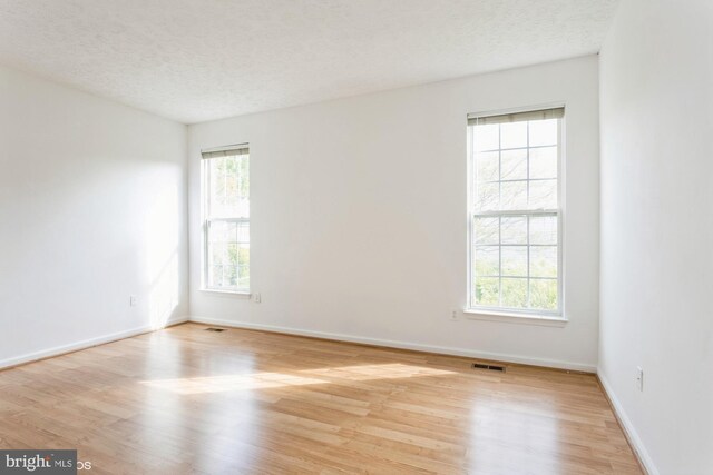 spare room with a textured ceiling, baseboards, visible vents, and wood finished floors