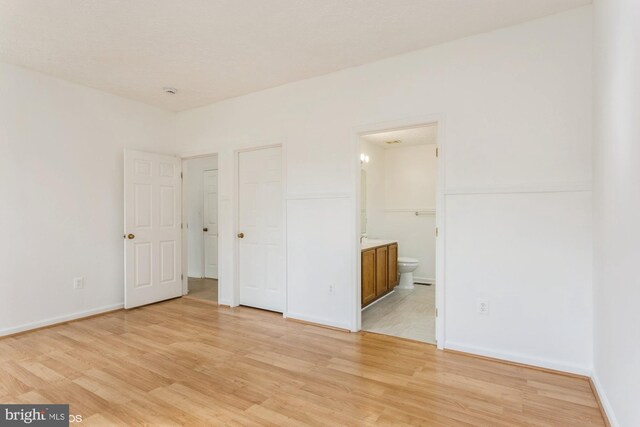unfurnished bedroom with connected bathroom, baseboards, and light wood-style floors