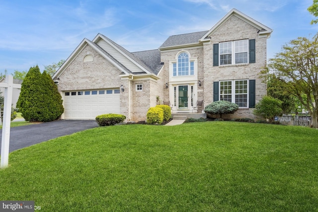 traditional-style house with a garage, a front yard, brick siding, and aphalt driveway