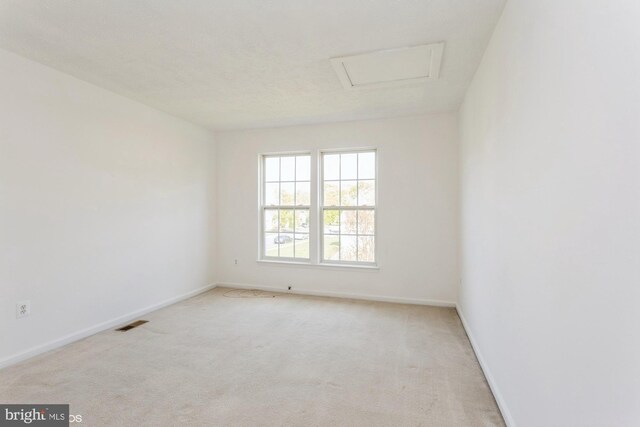 carpeted empty room with baseboards, attic access, and visible vents