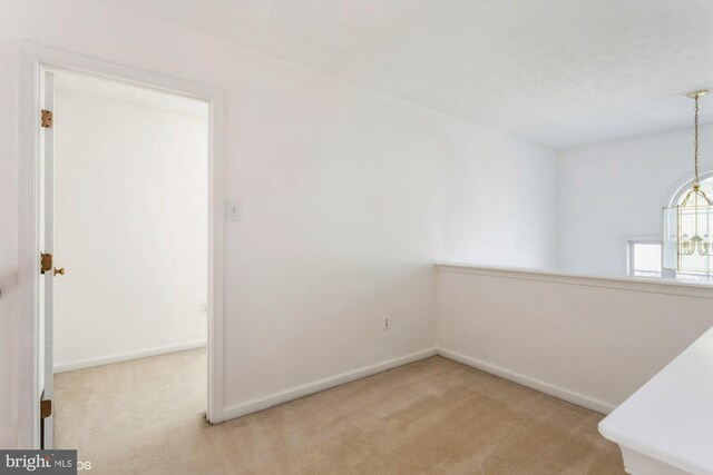 carpeted empty room featuring baseboards and a chandelier