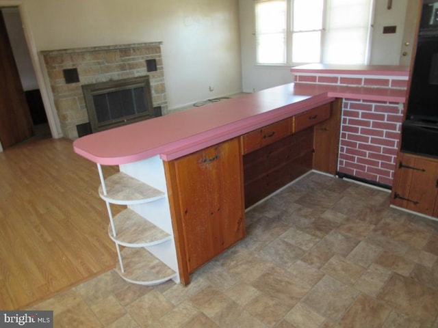 kitchen with a breakfast bar area, brown cabinetry, oven, a stone fireplace, and light countertops